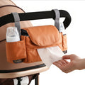 Universal stroller storage bag by Everything Baby with tissue pocket and cup holder, hanging on a stroller in brown.