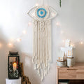 Beige large boho dream catcher with evil eye and macrame design hanging on wall, decorative bedroom or dorm room ornament.