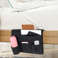 Dark gray bedside caddy organizer with four fabric pockets hanging from a bed or sofa, ideal for dorms and home use.