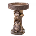 Antique-style resin raccoon birdbath in a garden, featuring a detailed raccoon figure, perfect for outdoor garden decor.